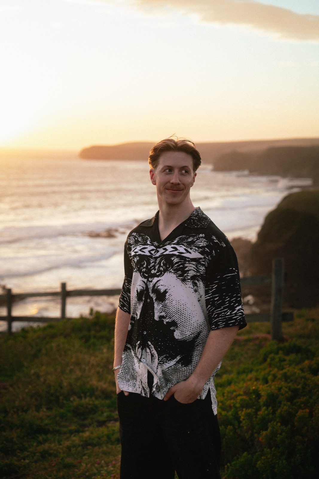 James Lewis, founder of hovr media, smiling on a clifftop above the ocean at sunset